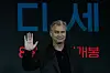 Christopher Nolan vinker foran en mørk bakgrunn med koreanske tegn.