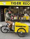 Syklist på lastesykkel foran en butikk med gult Tiger Records-skilt.