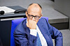 Friedrich Merz i blå dress sitter med hånden mot haken under en debatt i Forbundsdagen.
