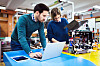 To studenter arbeider med en robotprototyp og bærbar datamaskin ved en arbeidsbenk.