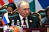 Vladimir Putin sitter ved Russlands plass under BRICS-toppmøtet, med flagg og blomster foran seg.