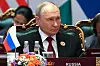 Vladimir Putin sitter ved Russlands plass under BRICS-toppmøtet, med flagg og blomster foran seg.
