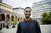Fawzi Warsame står foran historiske bygninger og et moderne kontorbygg i Oslo sentrum.