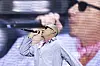 Macklemore rapper i stripete skjorte og solbriller på en festivalscene, med et stort nærbilde på skjermen bak.