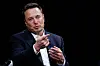 Elon Musk i mørk dress gestikulerer mot publikum foran en mørk bakgrunn.