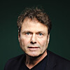 Nærbilde av en mann med brunt hår i mørk jakke mot grønn bakgrunn.
