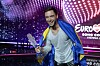 Måns Zelmerlöw smiler med Eurovision-pokalen og svensk flagg på scenen i Wien.