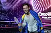 Måns Zelmerlöw smiler med Eurovision-pokalen og svensk flagg på scenen i Wien.