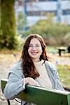 Smilende kvinne i lys jakke sitter på en grønn benk utendørs.