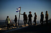 En gruppe mennesker står på en høyde ved solnedgang, med et israelsk flagg i vinden.