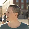 Profilportrett av en person med kort hår foran en uskarp bybakgrunn.