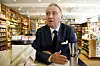 Terje Rød-Larsen i mørk dress sitter ved et bord foran bokhyller på Litteraturhuset.