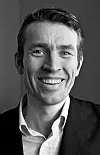 Svart-hvitt nærbilde av en smilende mann i dressjakke og skjorte.
