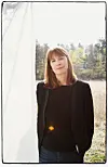 Kvinne i svart antrekk står foran et lyst tekstilstykke i et høstlig skoglandskap.