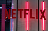 Rød Netflix-logo foran et mørkt, rutemønstret glassparti med vertikale lys.
