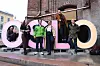 Gruppe mennesker foran store rosa, svarte og beige bokstaver ved en murbygning.