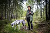 Hans Rustad med hatt på skogstur, med en flekket hund i forgrunnen.