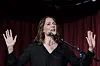 Åsne Seierstad står ved en mikrofon med hendene løftet foran en rød scenegardin.