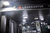 Mørk inngang med belyst skilt for Vinstra legekontor og glassdører inn til mottaket.