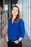 Helene Voldner i blå skjorte står i en lys gang med bokhyller i bakgrunnen.