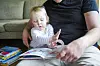 Barn og pappa leser en fargerik bok sammen i sofaen.