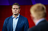 Harald Solberg står på en scene under en debatt, med en uskarp deltaker i forgrunnen.