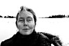 Portrett av Anne Carson i svart yttertøy ved en snødekt vannkant.