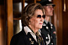 Dronning Sonja i mørk bekledning ved en treportal, med en uniformert vakt i bakgrunnen.