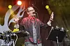 Mike Patton synger på scenen med armene hevet, omgitt av musikkanlegg og fargerike scenelys.