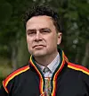 Portrett av Sigbjørn Skåden i fargerik samisk kofte foran en skog.