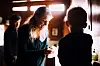Elizabeth Holmes står i sentrum i et dunkelt rom, med Nathan Fielder i bakgrunnen og en person nær kamera.