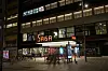 Opplyst fasade på nyoppussede Saga kino i Oslo, med sykler og mennesker utenfor på kveldstid.