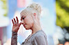 Phoebe Bridgers i profil med lyst hår og hånden løftet mot ansiktet på en rød løper.