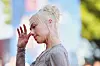 Phoebe Bridgers i profil med lyst hår og hånden løftet mot ansiktet på en rød løper.
