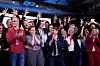 En stor gruppe studenter og medarbeidere jubler på en scene, mens en mann holder en mikrofon.