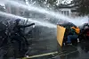 Demonstranter holder en treplate som skjold mens politiet spruter vann under en protest i Paris.