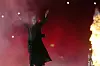 Ozzy Osbourne løfter armene på en rødlyst scene med flammer langs høyre side.